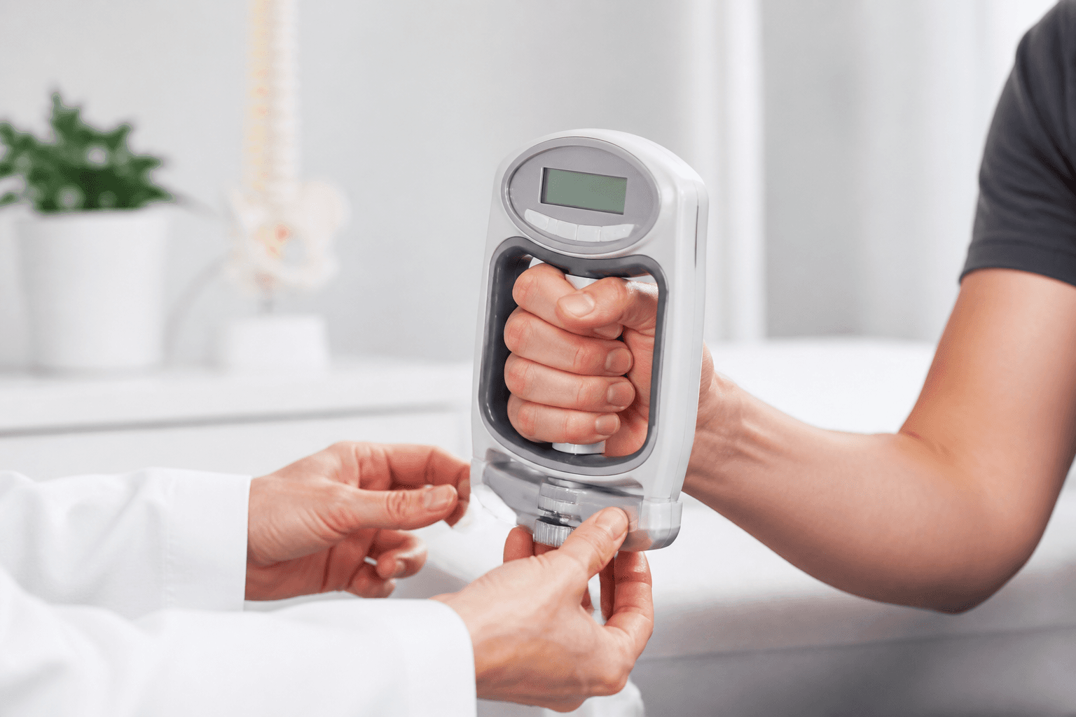 Close-up of hands demonstrating grip strength measurement with a modern handheld dynamometer, professional healthcare setting